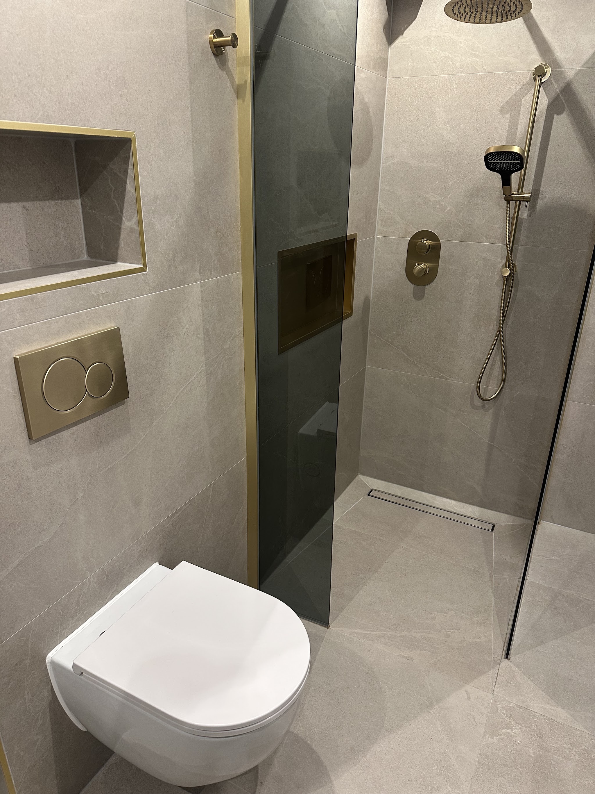 Afgewerkte inloopdouche met lichtgrijze marmerlook tegels, messing regendouche en hangtoilet