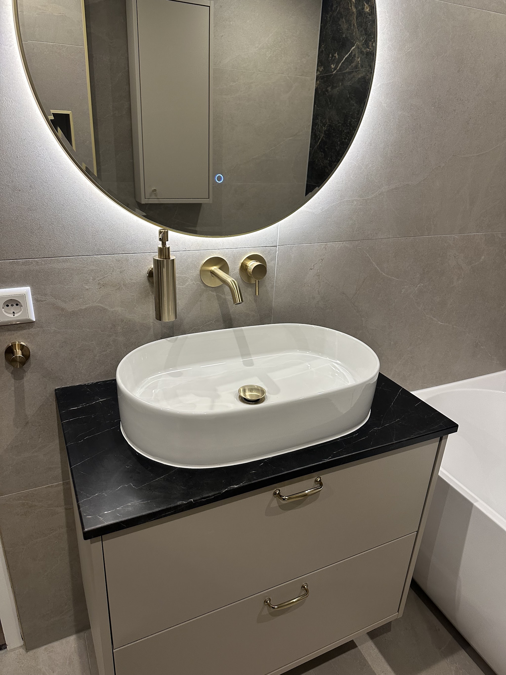 Wastafelmeubel met ronde verlichte spiegel, ovale opzetwastafel, messing wandkraan en zwart marmerlook blad