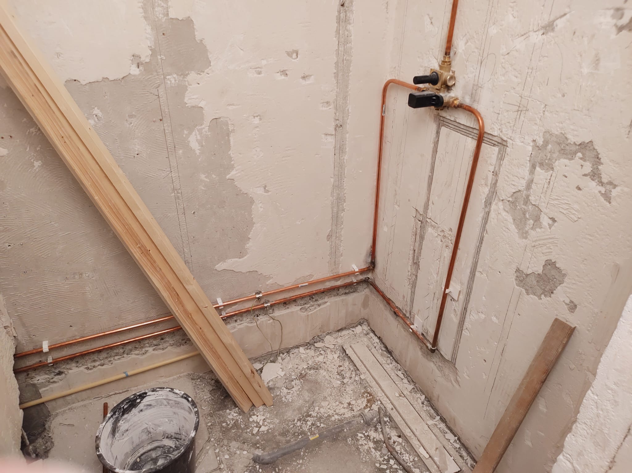 Gestripte badkamer met nieuwe koperen waterleidingen en houten regels, klaar voor de opbouw